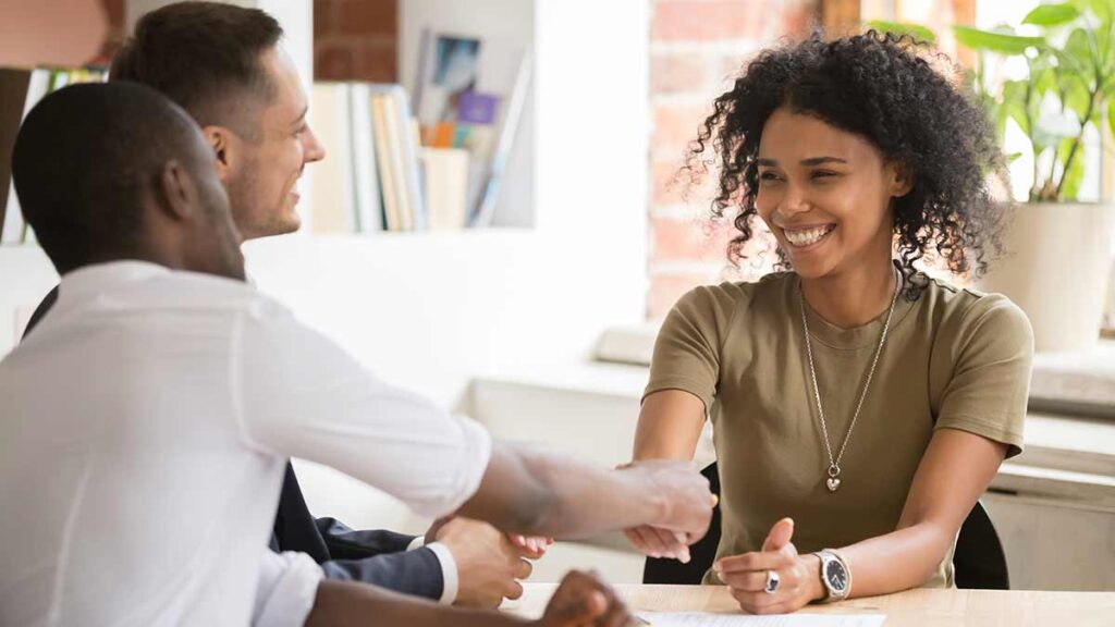 A smiling HR rep shakes hands with an employee in the company of an interpreter.