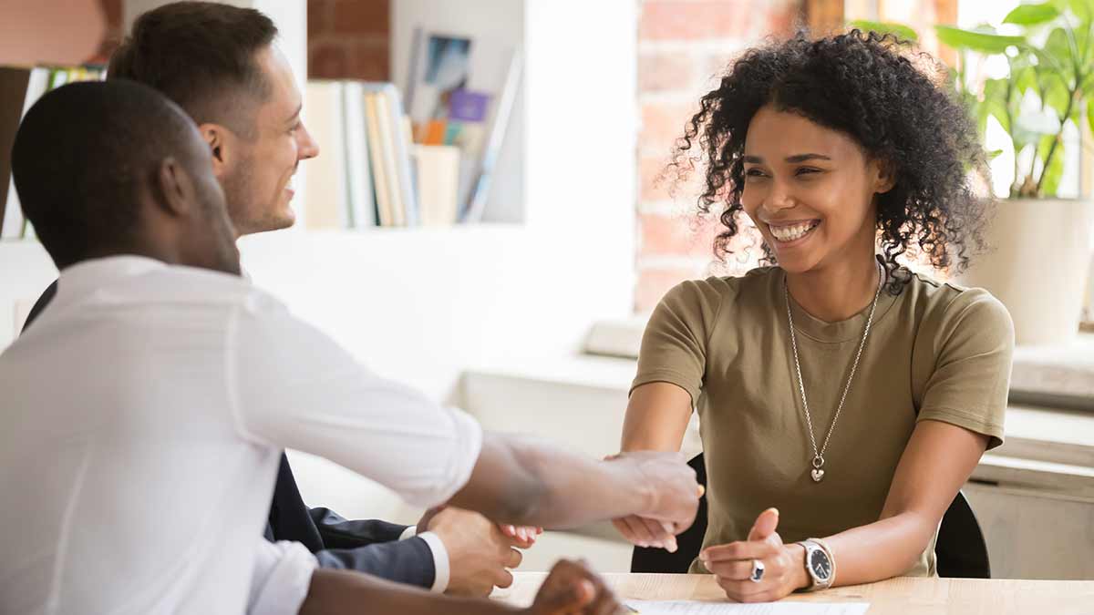 A smiling HR rep shakes hands with an employee in the company of an interpreter.