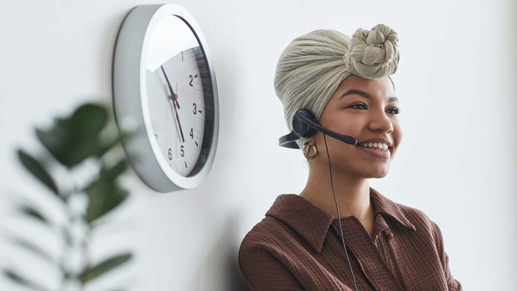 A remote interpreter wearing a headset smiles as they interpret for a deaf individual using a TTY device.