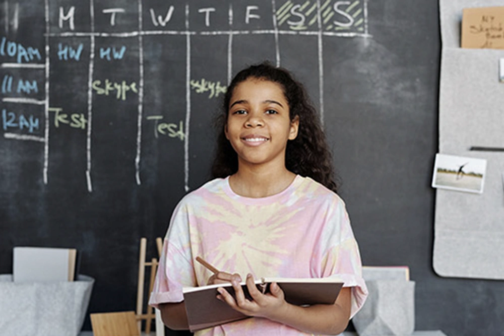 A non-English-speaking student writes in a notebook while their parents meet with a teacher and an interpreter.