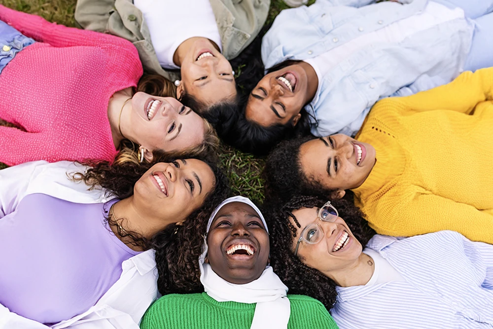 A diverse group of smiling employees relax in the grass together at a company picnic.