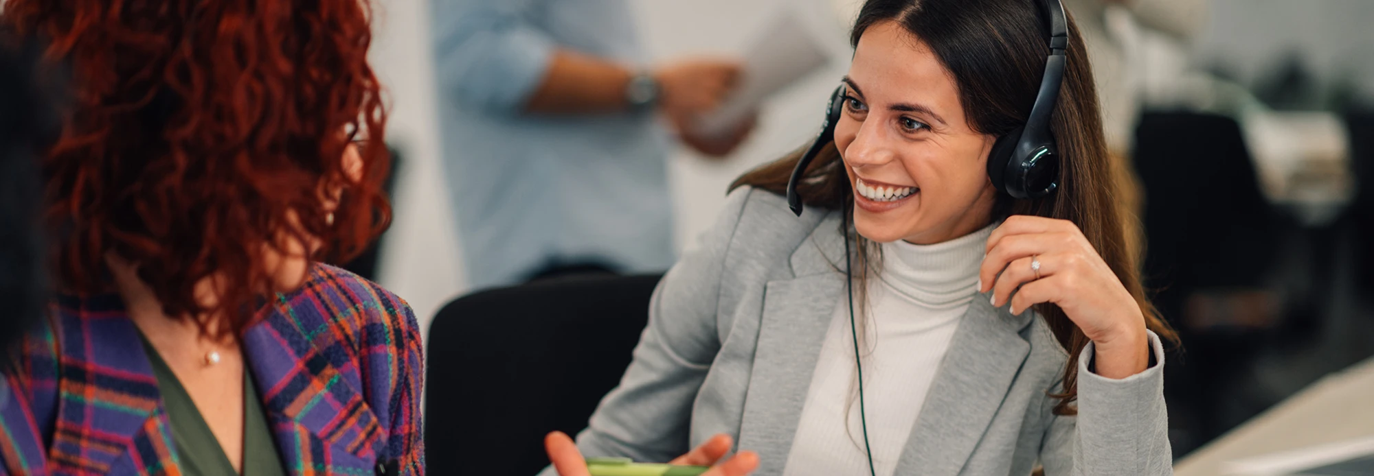 Two call center agents wearing headsets discuss the high quality of CLI's interpreting services.