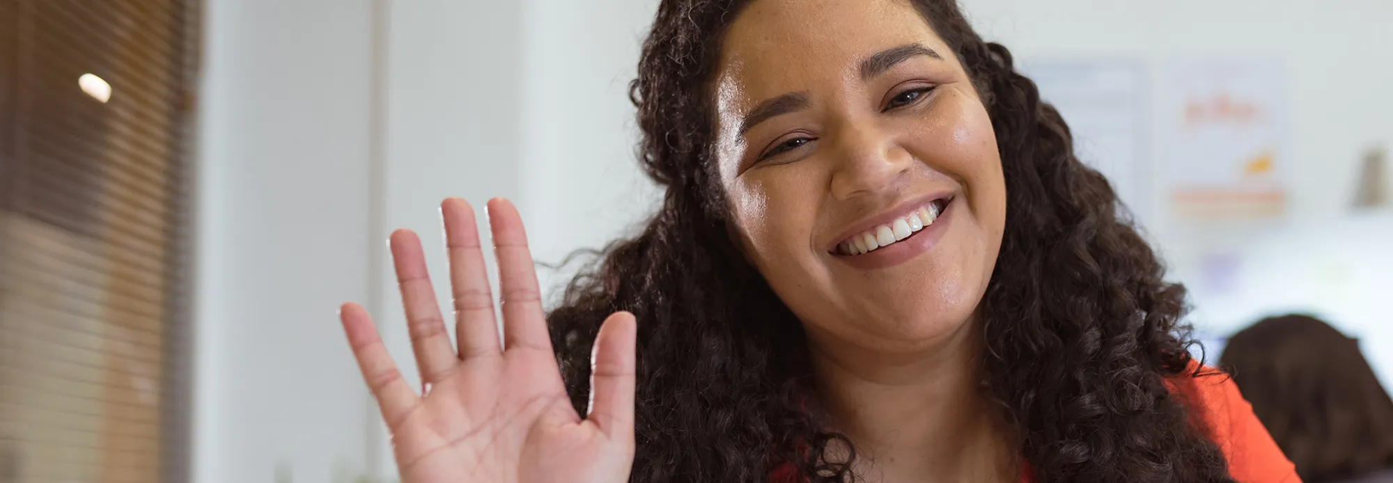 A Spanish interpreter answers a video call with a kind smile and a wave.